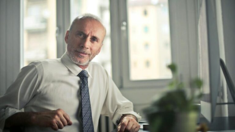 A mature man in professional attire smiling in an office setting.